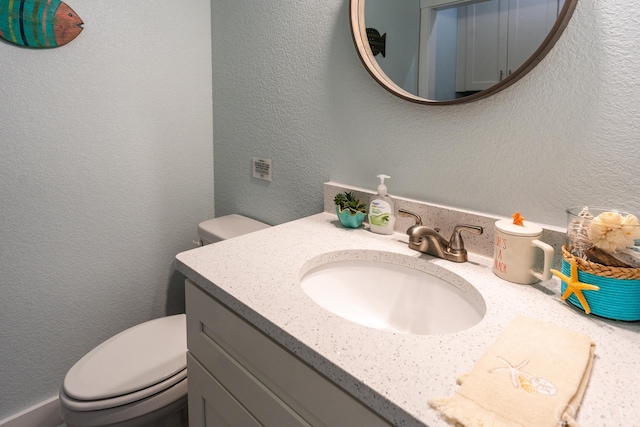 half bathroom with toilet, a textured wall, and vanity