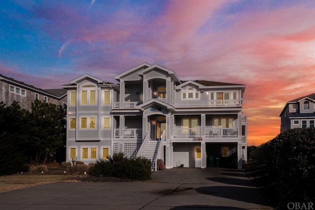 coastal inspired home with a porch, stairway, a balcony, a garage, and driveway