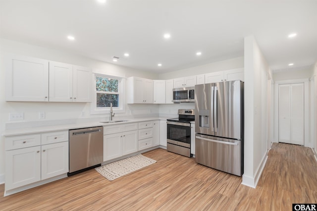 kitchen featuring a sink, stainless steel appliances, light wood-style floors, white cabinets, and light countertops