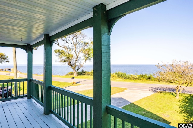 wooden deck featuring a water view, a lawn, and covered porch