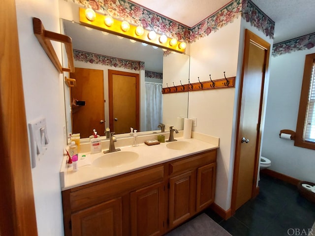 bathroom featuring double vanity, baseboards, toilet, and a sink