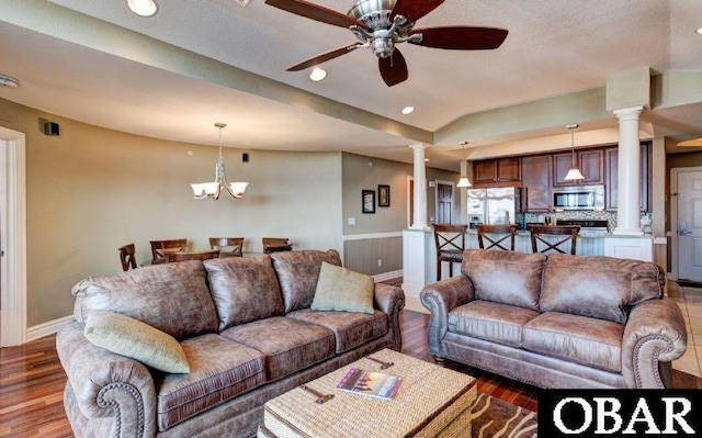 living area featuring ceiling fan with notable chandelier, a tray ceiling, wood finished floors, and ornate columns