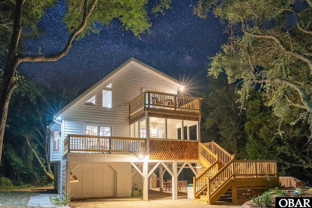 back of house at night with a garage, stairway, and a balcony