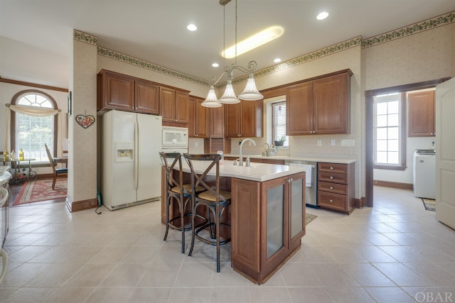 kitchen featuring white appliances, light countertops, wallpapered walls, an island with sink, and pendant lighting