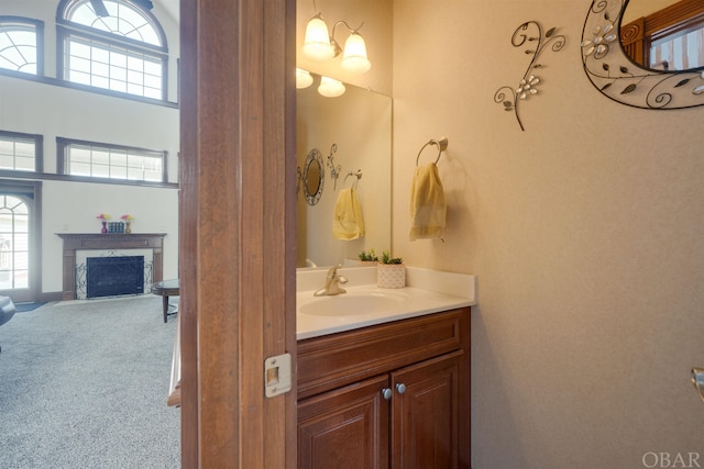 bathroom featuring a fireplace with flush hearth, vanity, and a high ceiling