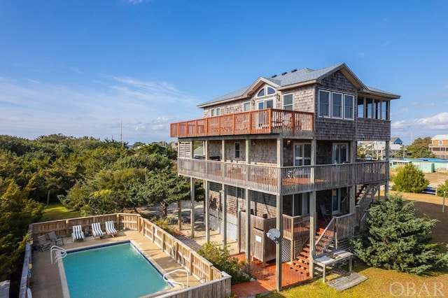 rear view of property with stairs, a patio area, a balcony, and a community pool