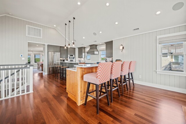 kitchen featuring stainless steel appliances, light countertops, custom range hood, visible vents, and a kitchen breakfast bar