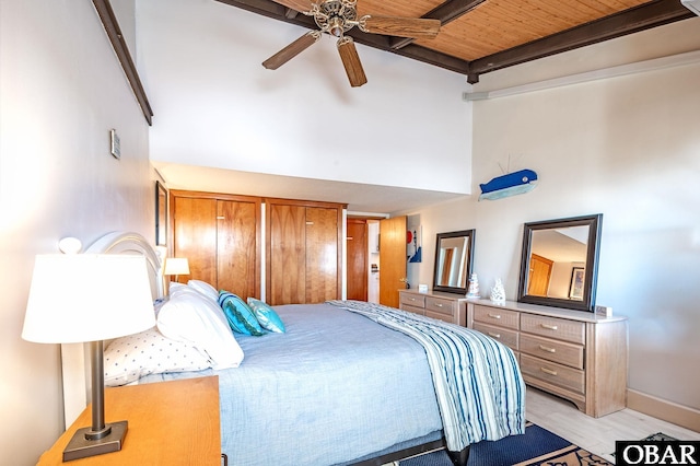 bedroom featuring light wood-style flooring, a high ceiling, a ceiling fan, baseboards, and beam ceiling