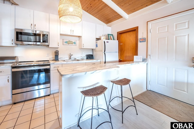 kitchen with a peninsula, appliances with stainless steel finishes, a breakfast bar, and white cabinetry