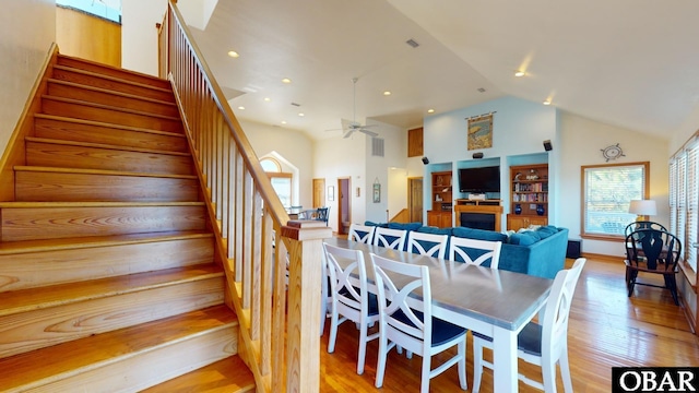 dining area with stairs, wood finished floors, a fireplace, and high vaulted ceiling