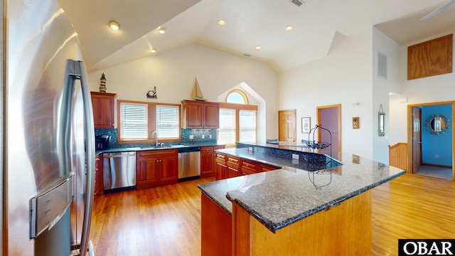 kitchen featuring backsplash, light wood-style flooring, appliances with stainless steel finishes, high vaulted ceiling, and a sink