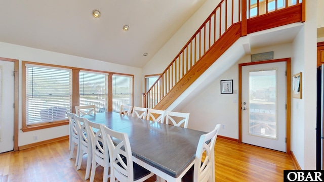 dining area featuring baseboards, high vaulted ceiling, stairs, and light wood-style floors