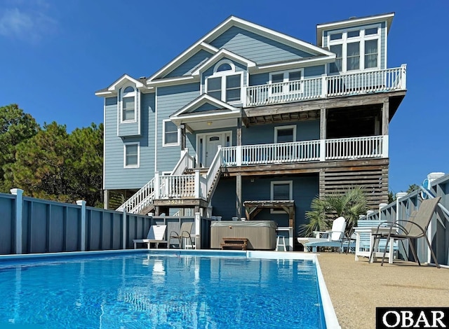 back of house featuring a balcony, stairway, a fenced in pool, fence, and a hot tub