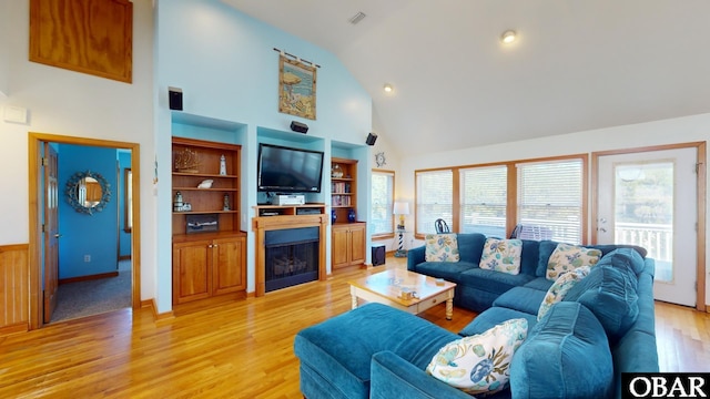 living area with light wood finished floors, visible vents, a fireplace, and high vaulted ceiling