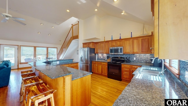 kitchen featuring a breakfast bar area, brown cabinetry, a sink, stainless steel appliances, and light wood-style floors