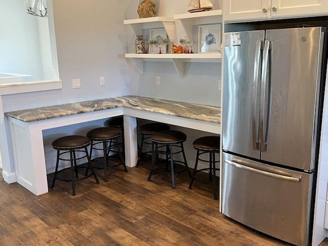 kitchen featuring dark wood-type flooring, stone countertops, freestanding refrigerator, and white cabinets