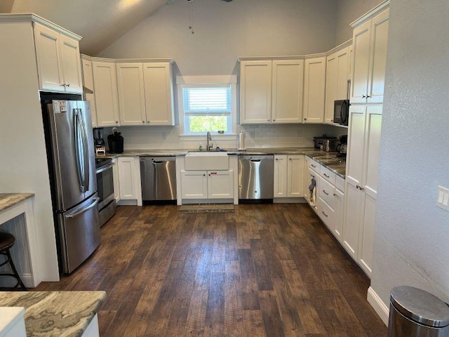 kitchen with white cabinets, dark wood finished floors, lofted ceiling, stainless steel appliances, and a sink