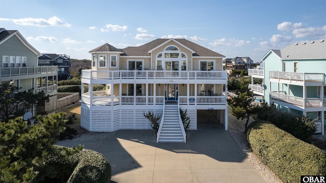 view of front facade with driveway, a balcony, a residential view, roof with shingles, and stairs