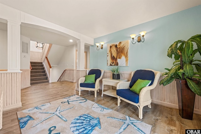 living area with stairway, wood finished floors, and ornate columns