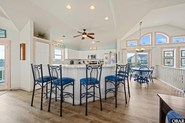 kitchen with light wood finished floors, white cabinets, light stone counters, stainless steel appliances, and a kitchen bar