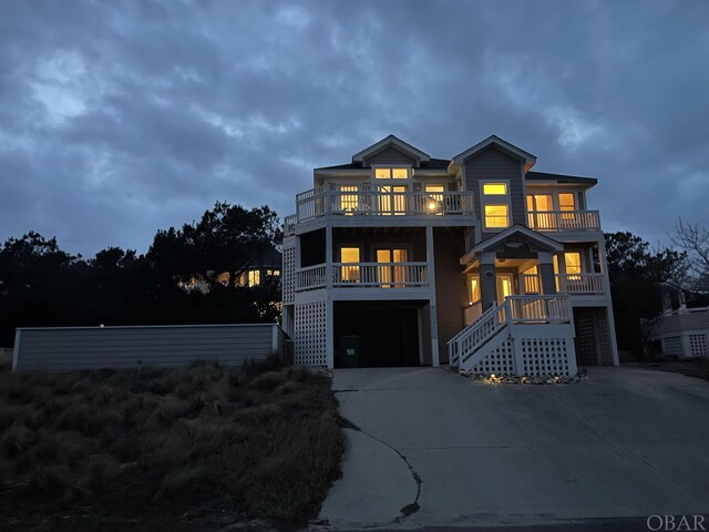 raised beach house with a garage, concrete driveway, a balcony, and stairs