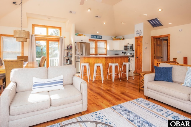 living room with light wood-type flooring, high vaulted ceiling, visible vents, and recessed lighting