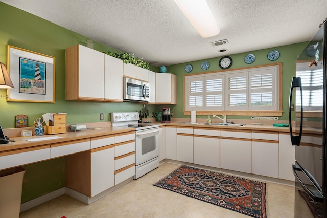 kitchen with white range with electric stovetop, light countertops, stainless steel microwave, freestanding refrigerator, and white cabinets