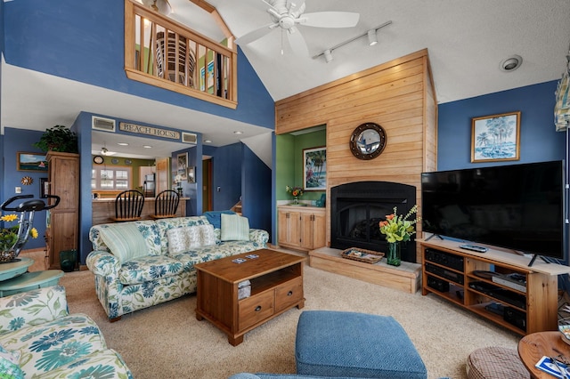 living area featuring a fireplace with raised hearth, a ceiling fan, carpet flooring, wood walls, and track lighting