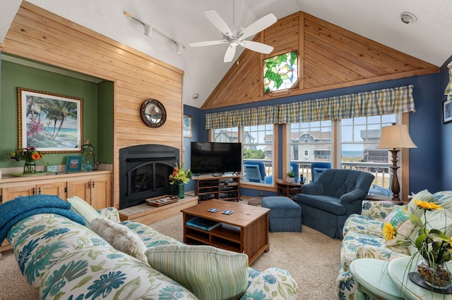 living area featuring a fireplace with raised hearth, a ceiling fan, light carpet, wooden walls, and track lighting