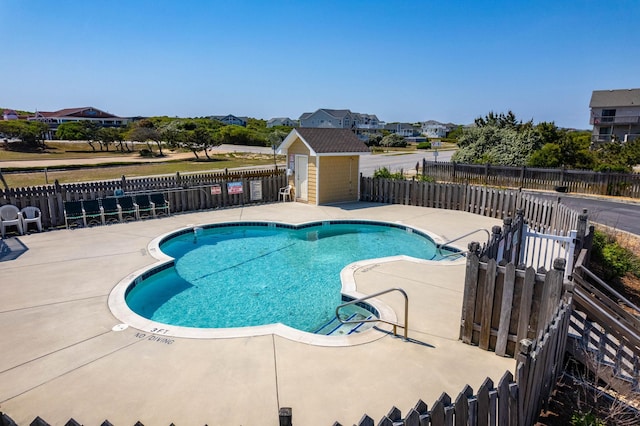 pool with a patio area, a storage shed, fence, and an outbuilding