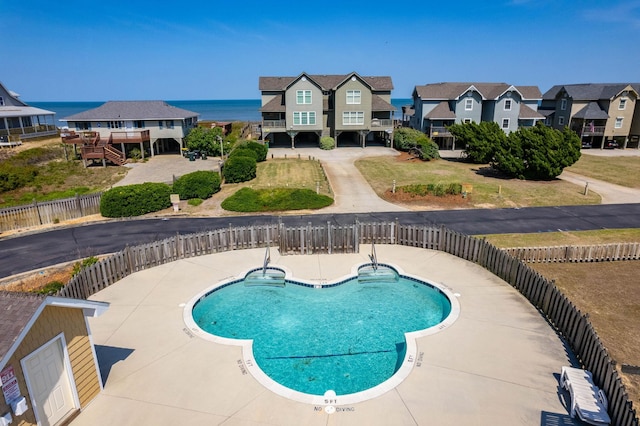 pool featuring a water view, a residential view, fence, and a patio