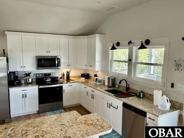 kitchen featuring decorative backsplash, lofted ceiling, white cabinets, a sink, and appliances with stainless steel finishes