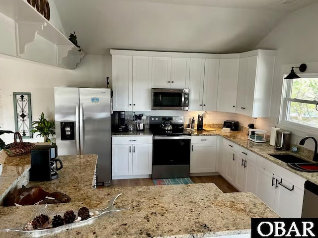 kitchen with decorative backsplash, white cabinets, a sink, vaulted ceiling, and stainless steel appliances
