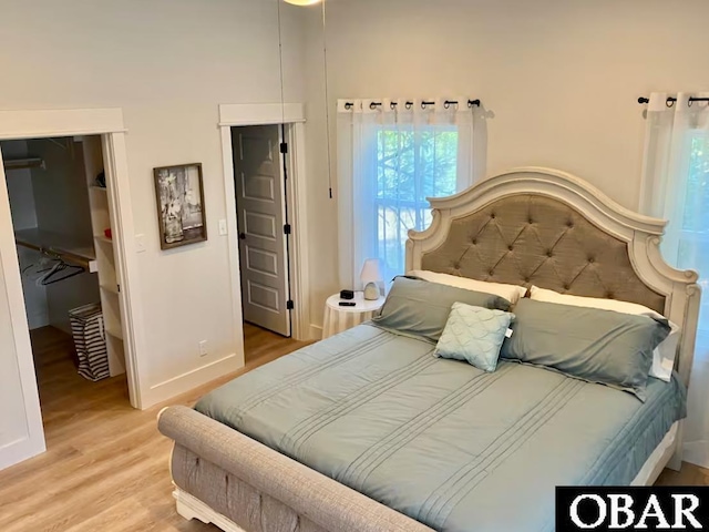 bedroom featuring a closet, baseboards, a walk in closet, and light wood-style floors