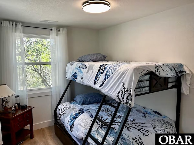 bedroom with baseboards, multiple windows, wood finished floors, and visible vents