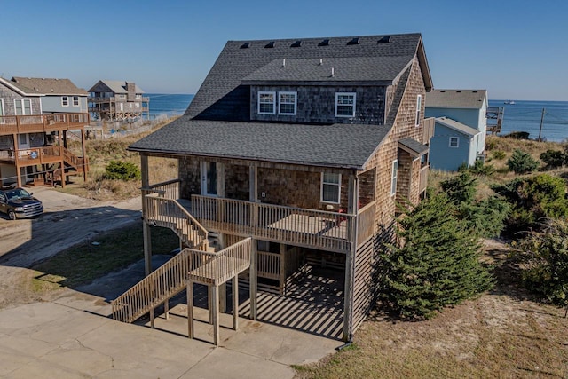 rear view of house with a water view, covered porch, a shingled roof, and stairway