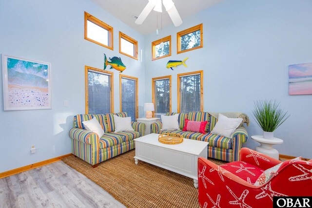 living area featuring ceiling fan, a high ceiling, wood finished floors, and baseboards