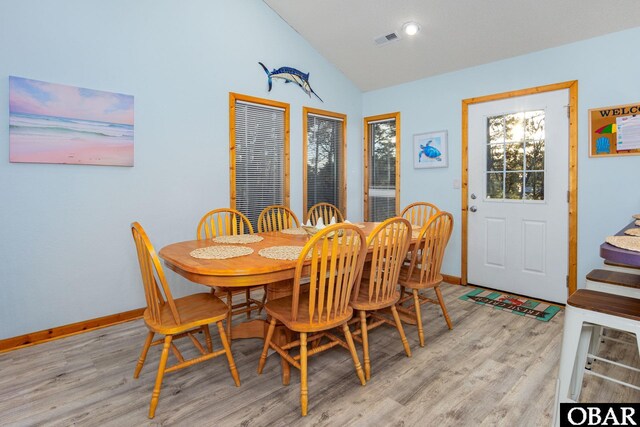 dining area with light wood-type flooring, visible vents, vaulted ceiling, and baseboards