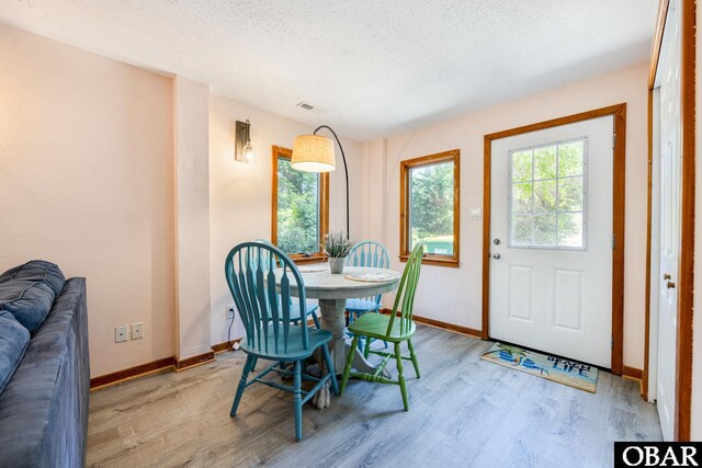 dining area featuring a textured ceiling, light wood finished floors, visible vents, and baseboards