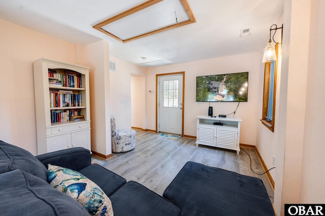 living area featuring light wood finished floors, attic access, visible vents, and baseboards