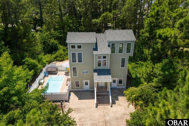 view of front of home with roof with shingles, an outdoor pool, fence, and a patio