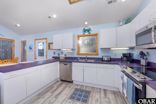 kitchen with appliances with stainless steel finishes, dark countertops, a sink, and white cabinets