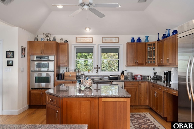 kitchen featuring appliances with stainless steel finishes, dark stone countertops, a kitchen island, and glass insert cabinets