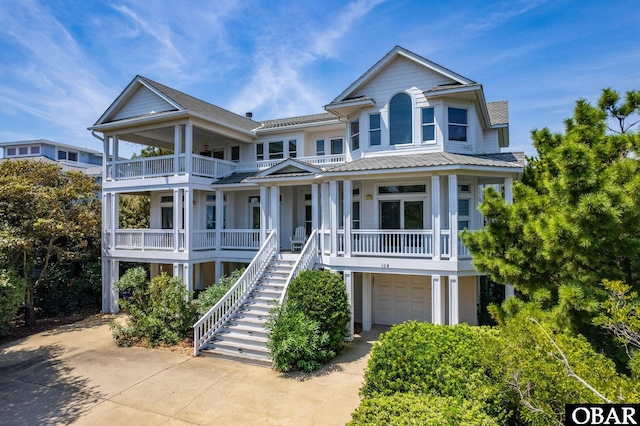 coastal home featuring concrete driveway, covered porch, an attached garage, and stairs