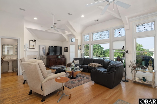 living area featuring a fireplace, light wood finished floors, visible vents, ceiling fan, and high vaulted ceiling