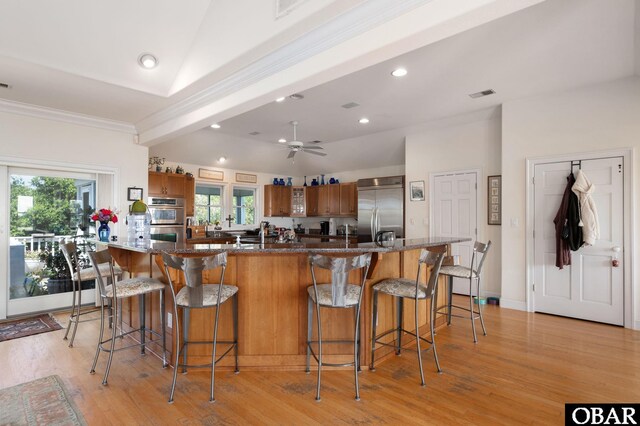 kitchen featuring visible vents, appliances with stainless steel finishes, a kitchen breakfast bar, ornamental molding, and light wood-style floors