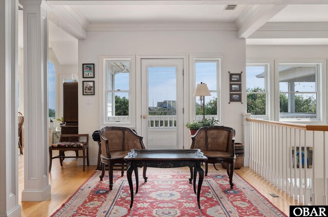 sitting room with wood finished floors, visible vents, beam ceiling, ornate columns, and crown molding