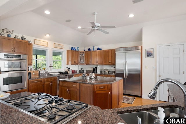 kitchen featuring a sink, appliances with stainless steel finishes, a center island, brown cabinetry, and glass insert cabinets