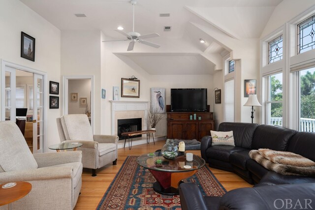 living room featuring light wood-type flooring, high vaulted ceiling, a fireplace, and visible vents