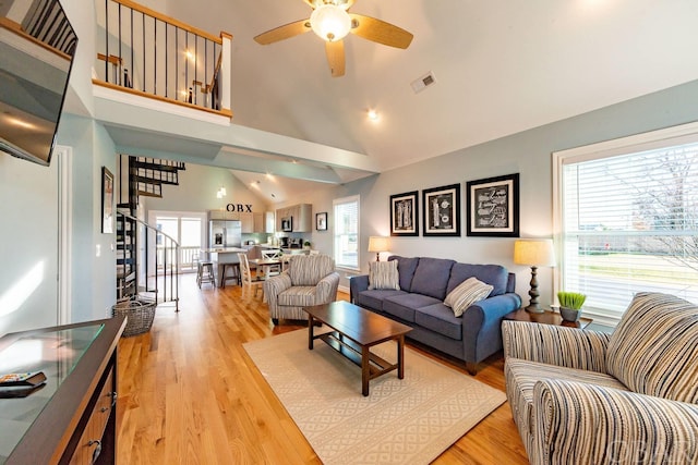 living area featuring high vaulted ceiling, visible vents, light wood-style flooring, and stairs